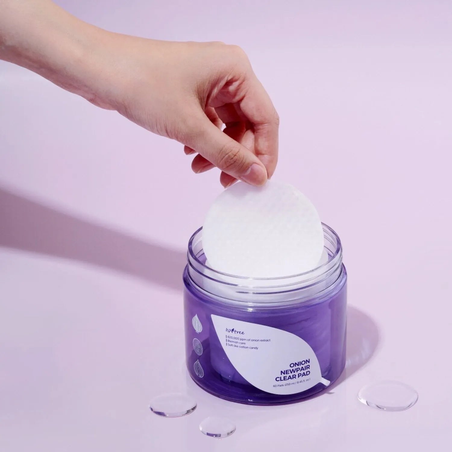 Hand reaching into a Isntree Onion Newpair Clear Pad jar to take out a white cleaning pad 